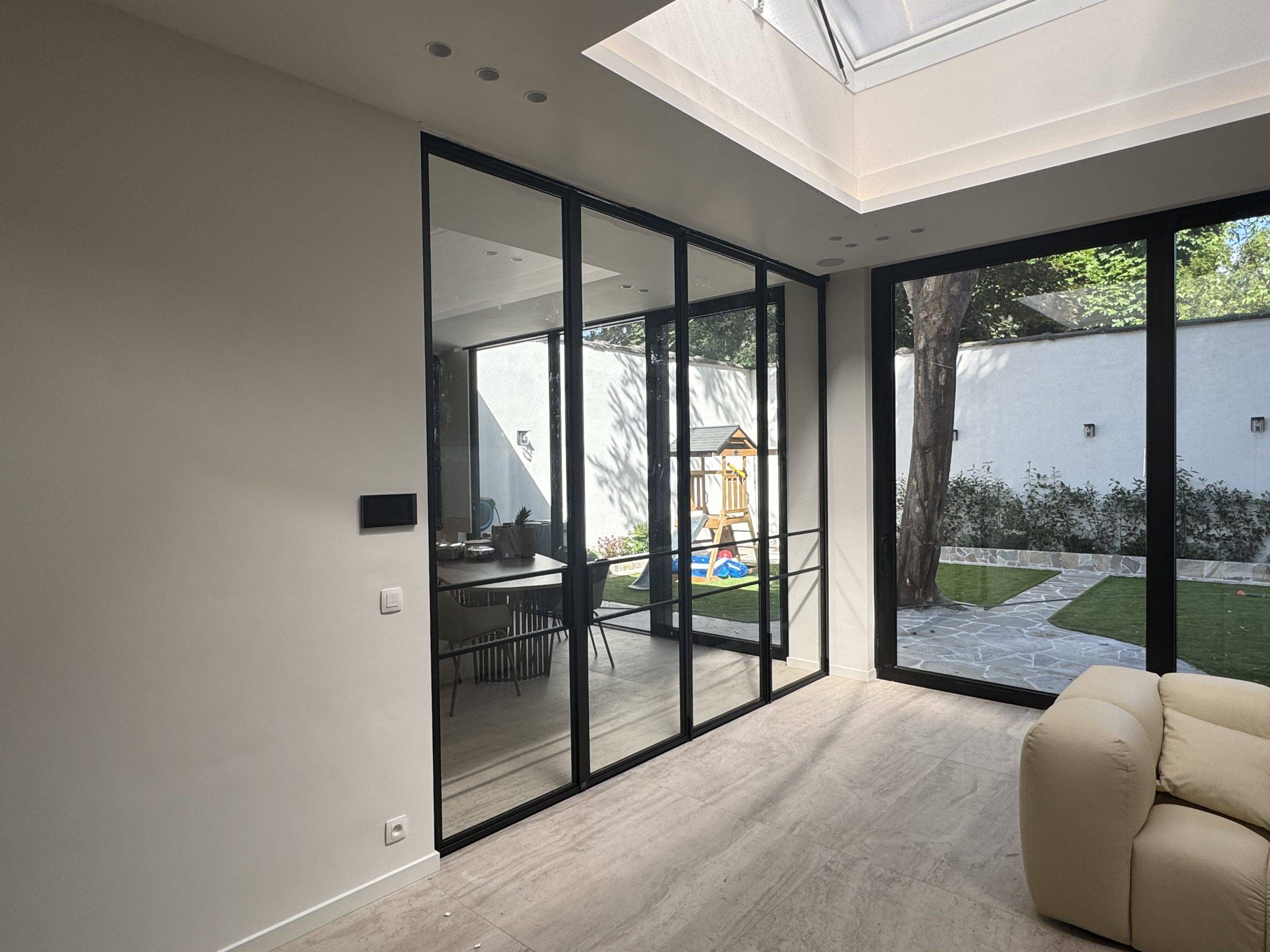 Modern interieur met glazen wand en uitzicht op groene tuin en gezellige zithoek.