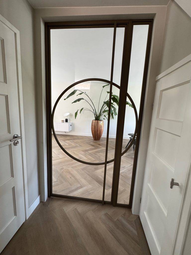 Moderne interieur met glazen deur, houten vloer en groene plant in terracotta pot.