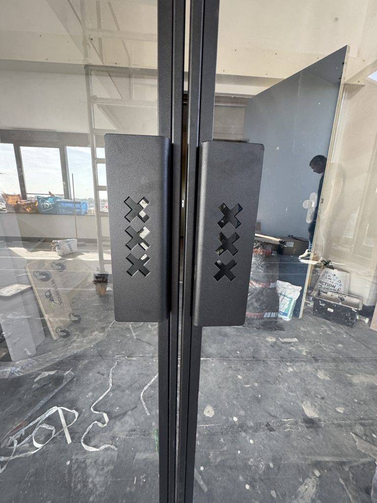 Moderne glazen deur met zwart metalen handgreep en X-motieven in een onder constructie ruimte.