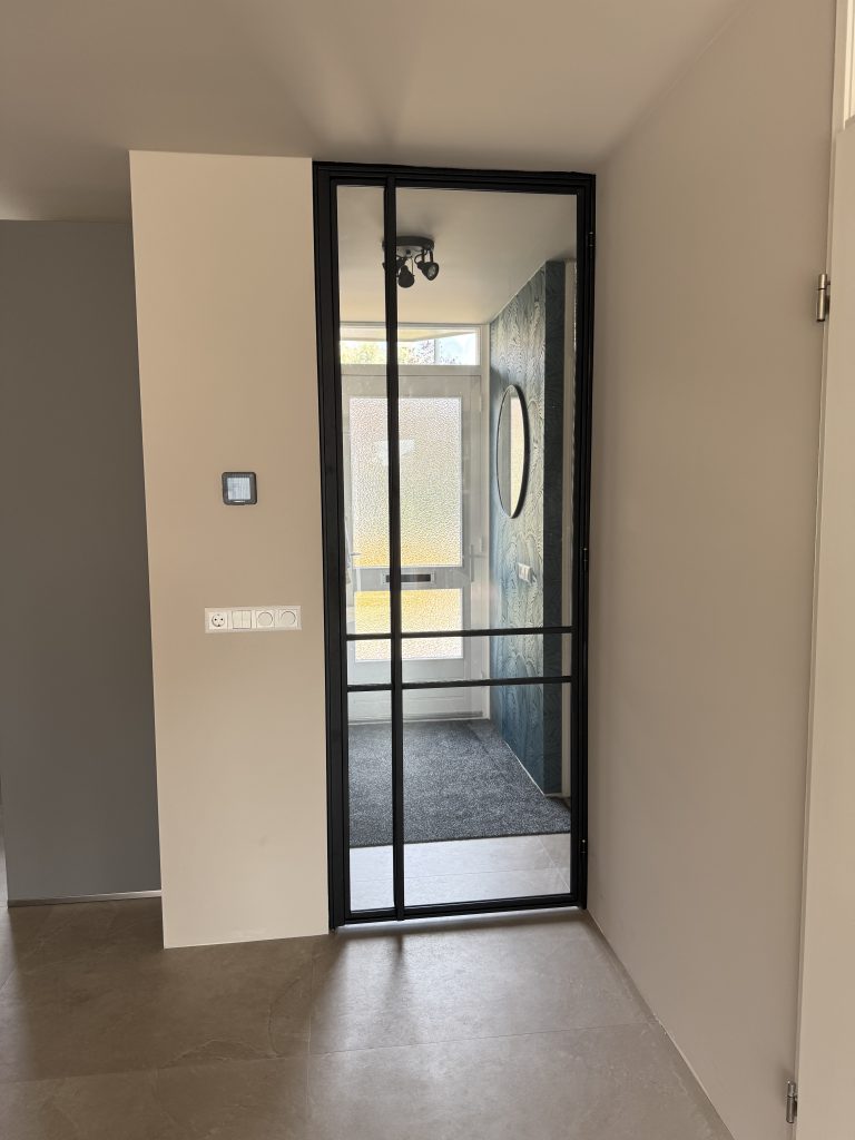 Moderne entree met glazen deur, ronde spiegel en lichte, minimalistische inrichting.