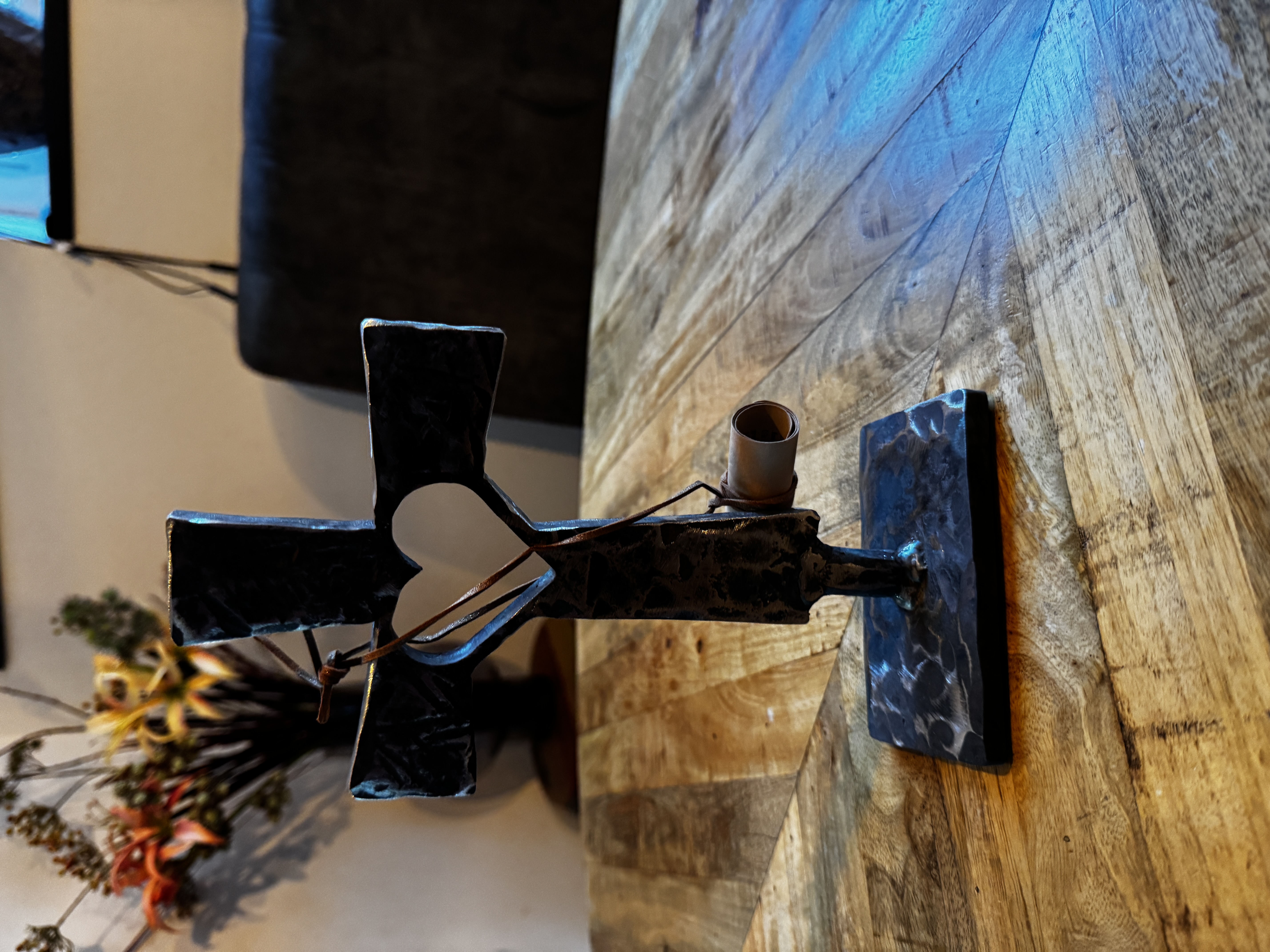 Decoratief metalen kruis met hartuitsnijding en kaars, op houten tafel met bloemen en warme sfeer.