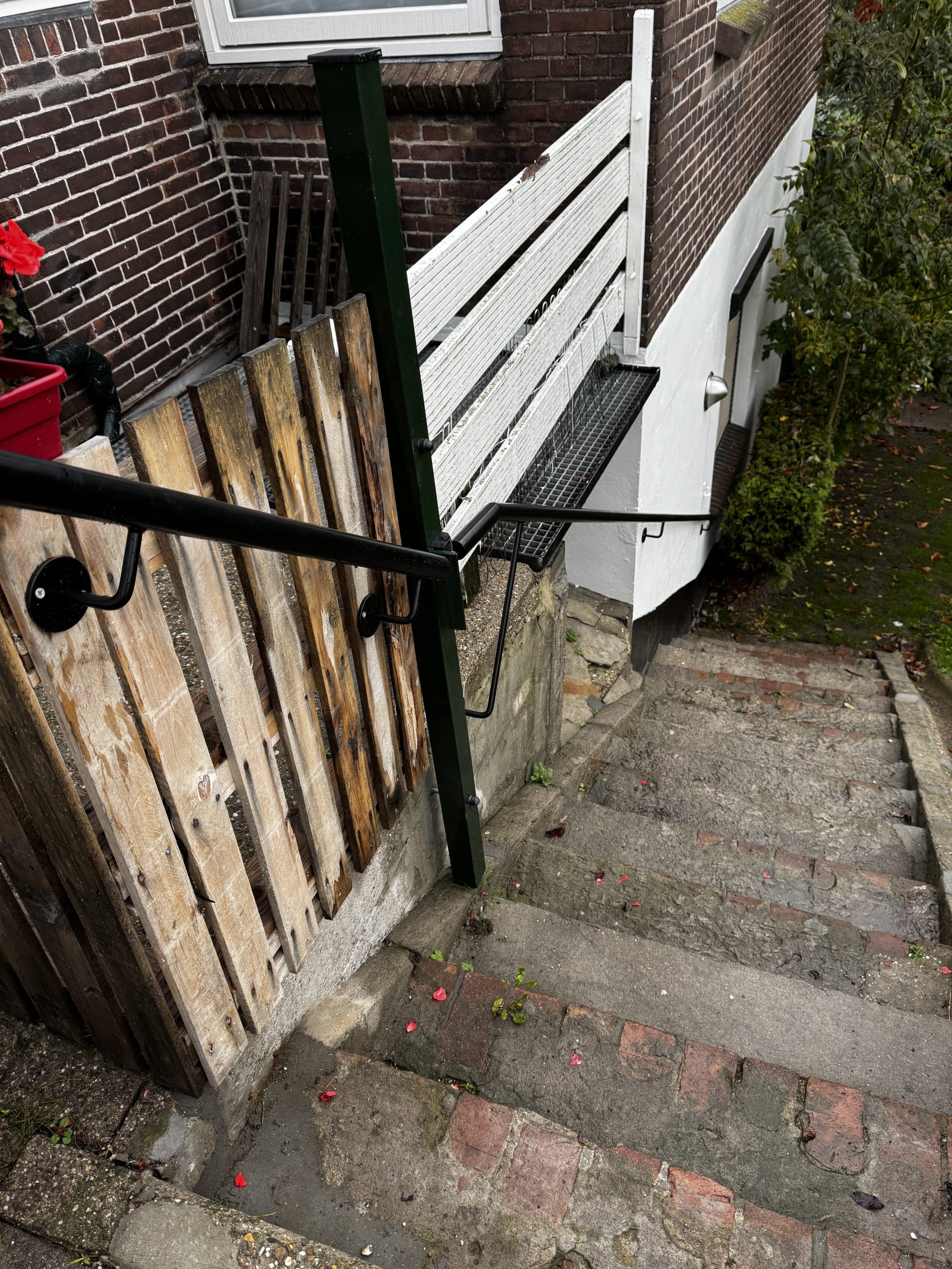 Buitentrap met houten hek, rode bloemen en witte deur in rustige tuinomgeving