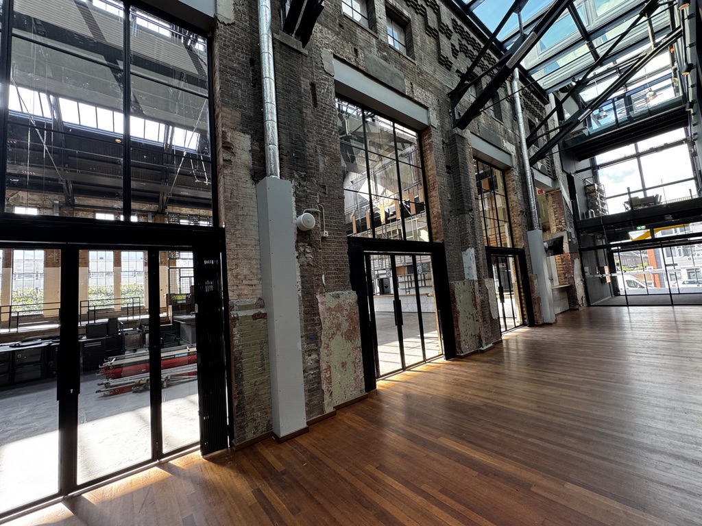 Modern industrieel interieur met glazen dak, bakstenen muren, houten vloeren en grote raampartijen.