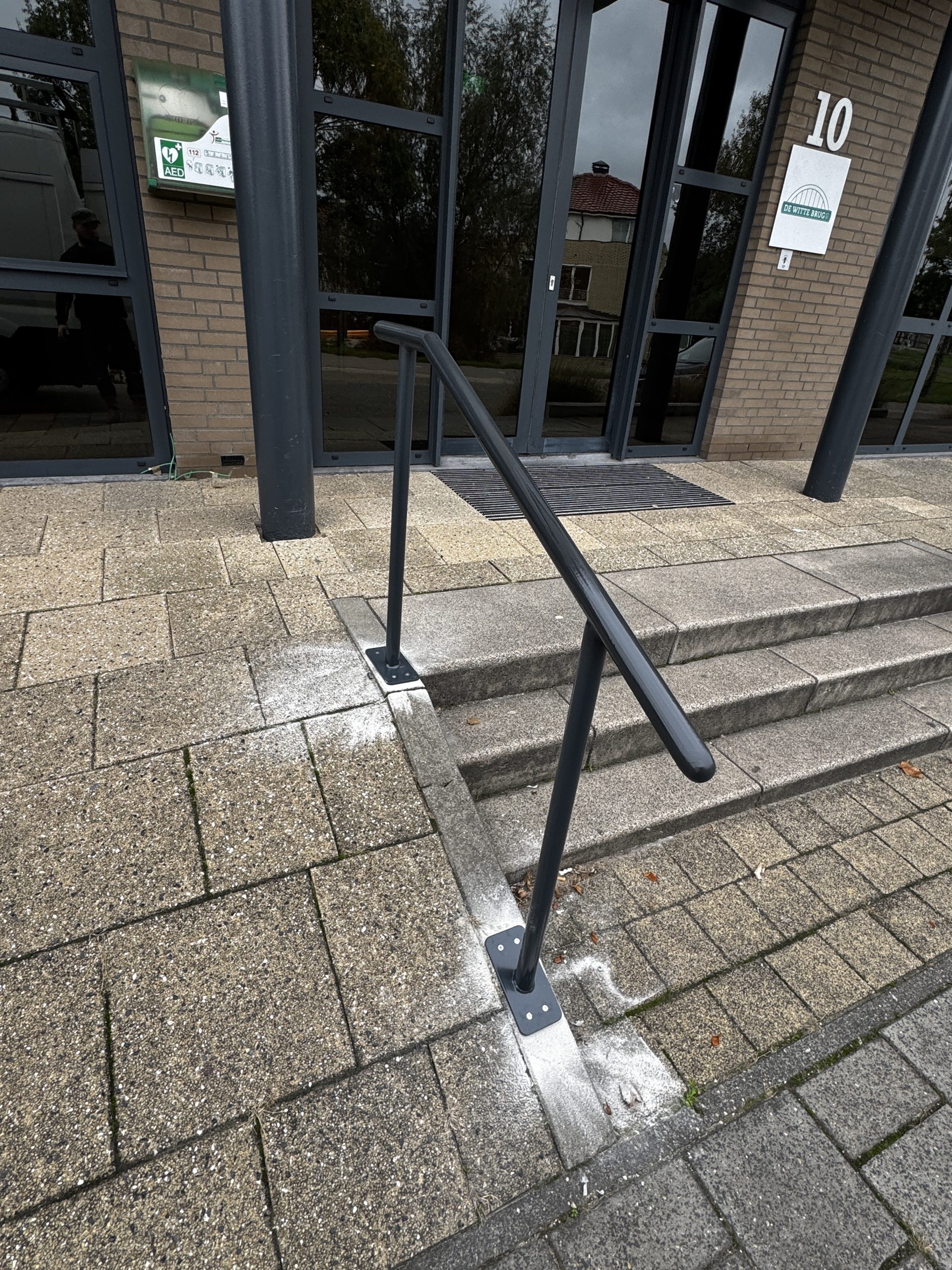 Stappen naar gemeentegebouw met glazen deuren, metalen leuning en moderne, onderhouden uitstraling.