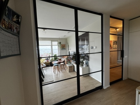 Modern interieur met glazen deuren, natuurlijke lichtinval, gezellige zithoeken en groene planten.