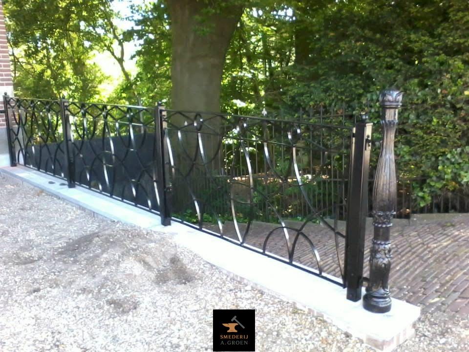 Zwart hekwerk bij een tuin.